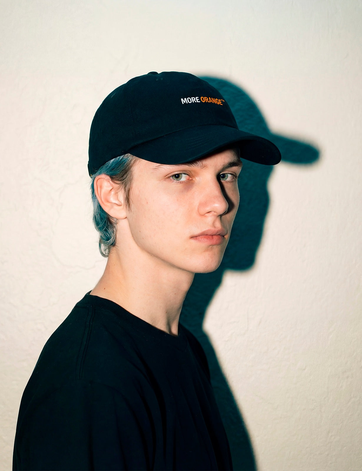 Front-side view of a male model wearing a black MORE ORANGE™ dad hat in a minimalist streetwear look