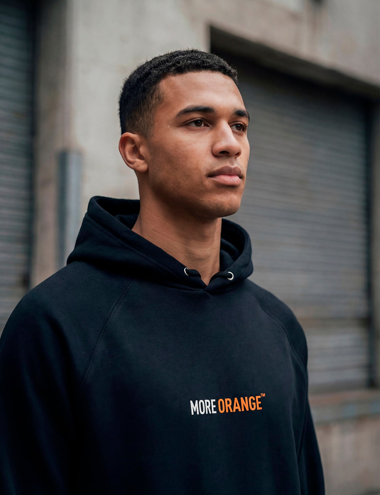 Male model wearing black MORE ORANGE™ hoodie photographed in urban concrete setting