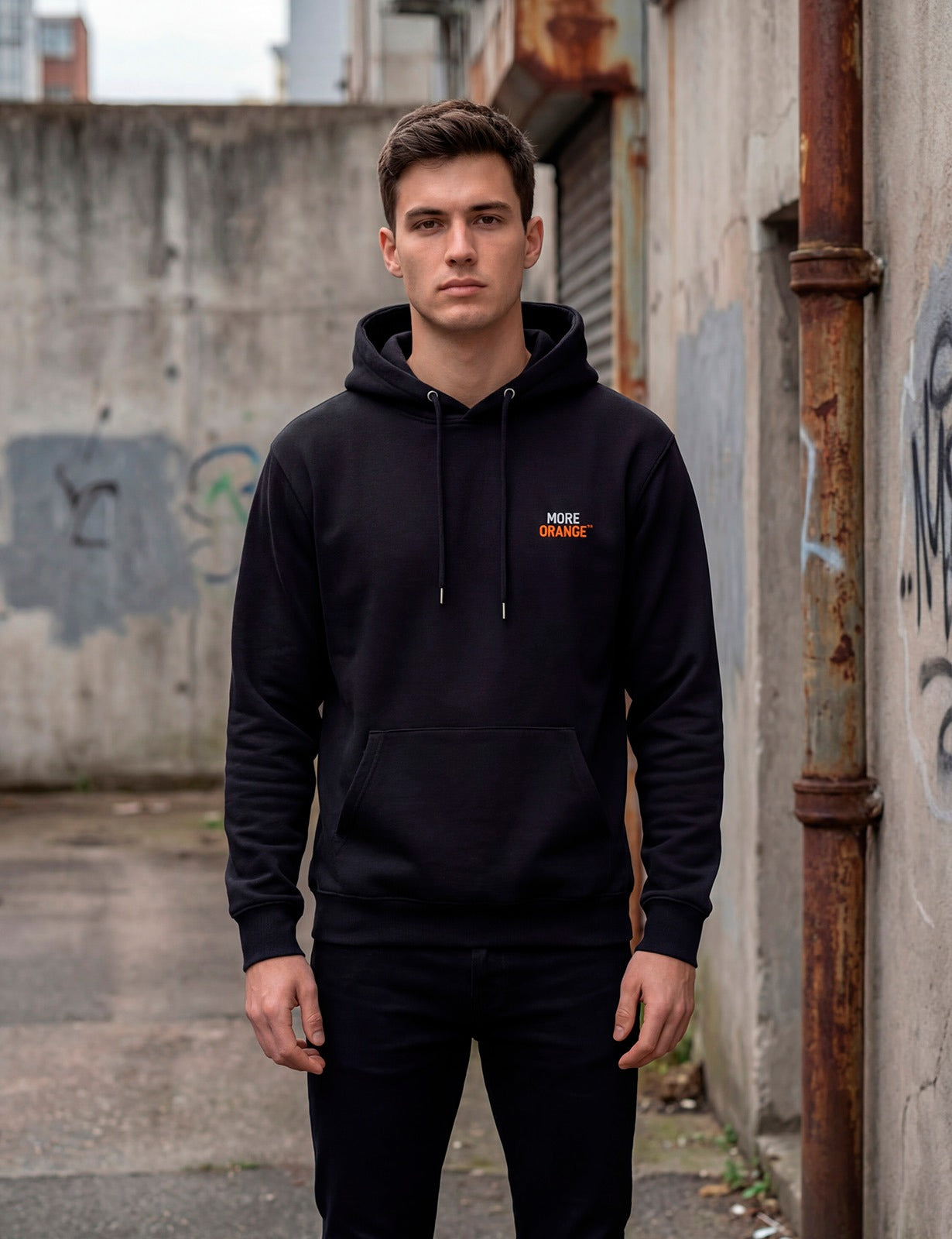 Full body front view of male model wearing black MORE ORANGE™ hoodie in urban environment