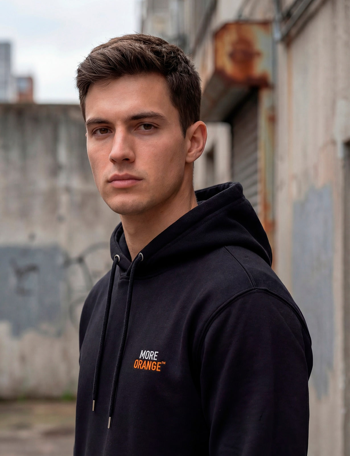 Close-up side view of male model wearing black MORE ORANGE™ hoodie in urban setting