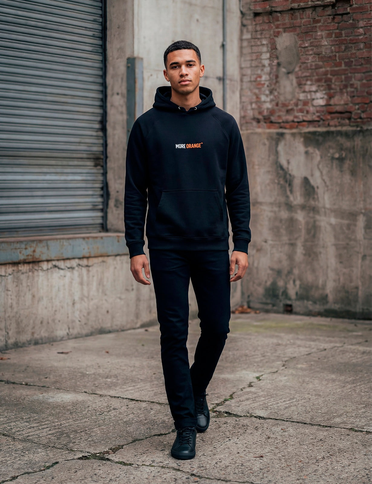 Male model in black MORE ORANGE™ hoodie photographed in an urban street setting
