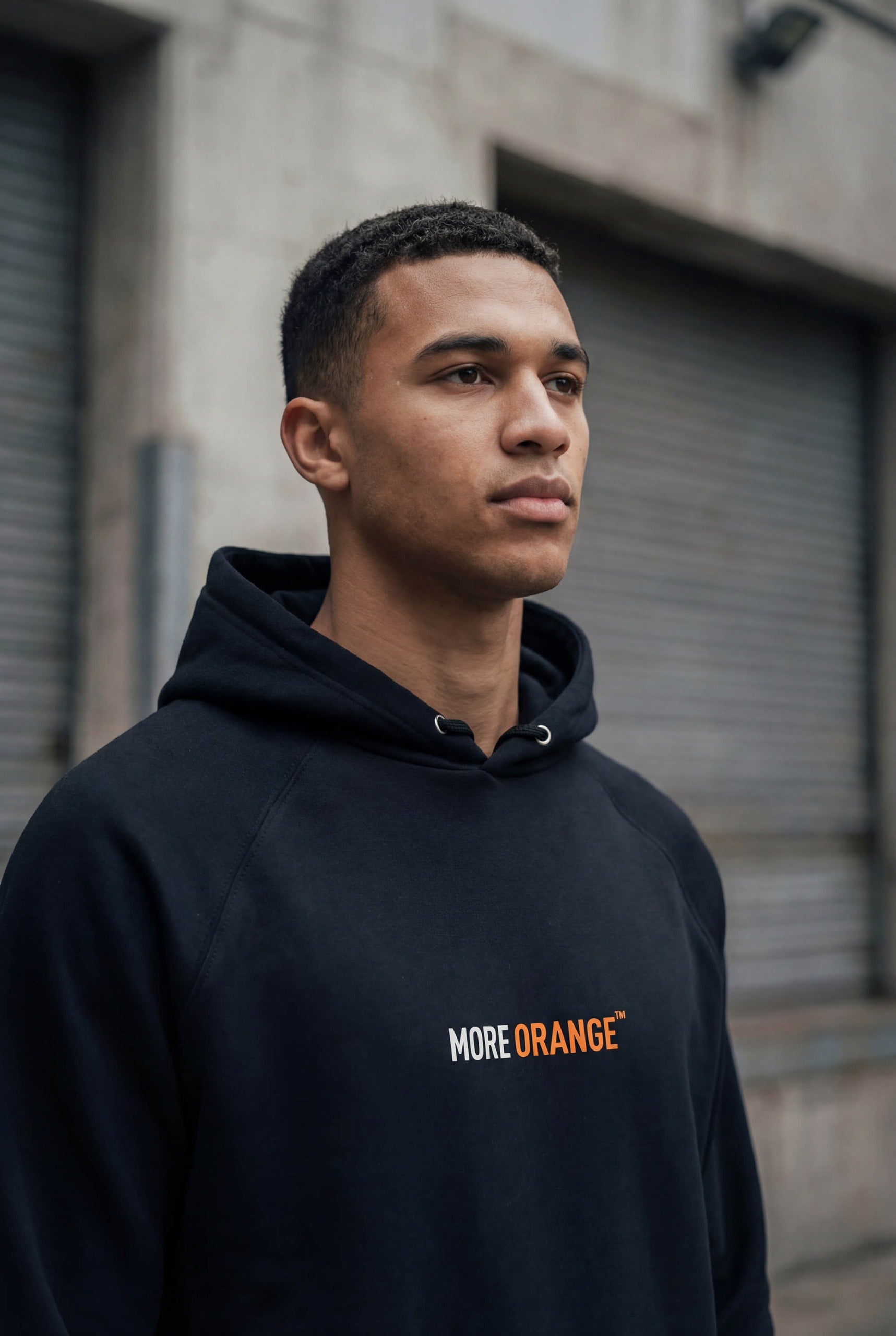 Front view of black MORE ORANGE™ hoodie styled in an urban street setting