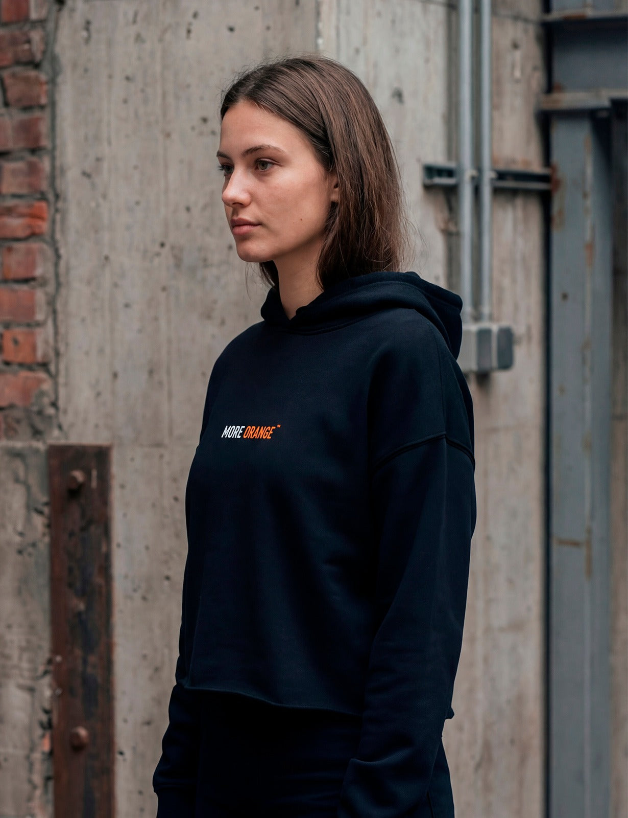 Half-side view of female model wearing black MORE ORANGE™ hoodie with clean design