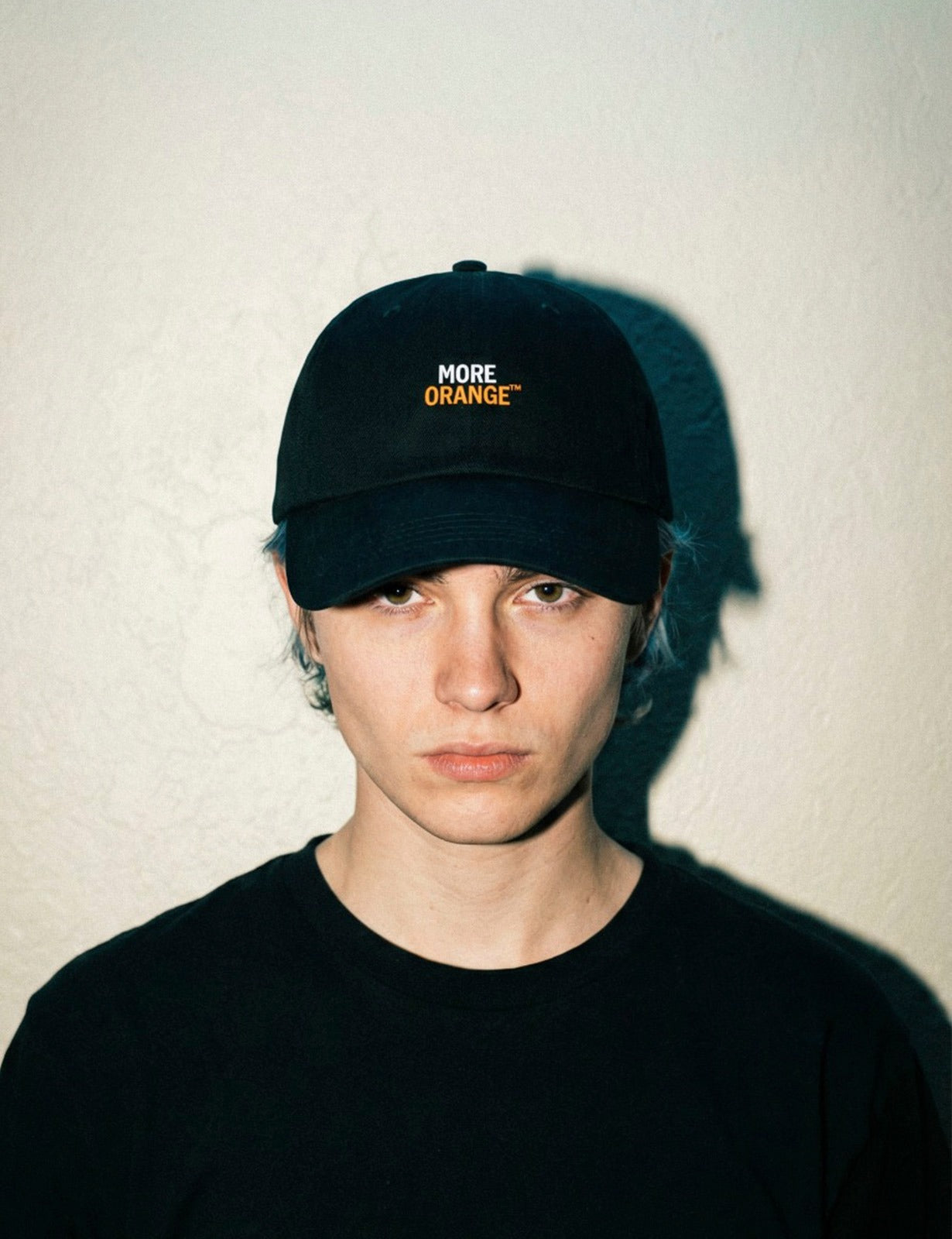 Front view of young male model wearing black MORE ORANGE™ dad hat with orange embroidery